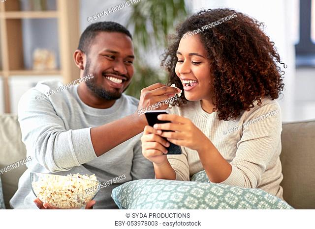 african couple with popcorn and smartphone at home