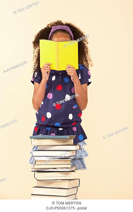 Young girl reading by a stack of books indoors