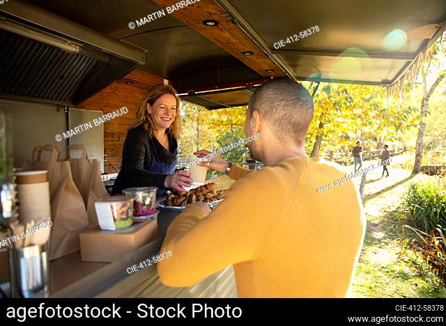 Friendly food cart owner serving coffee to customer in autumn park