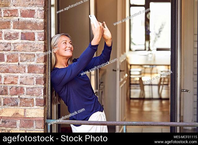 Smiling woman taking selfie through smart phone in balcony