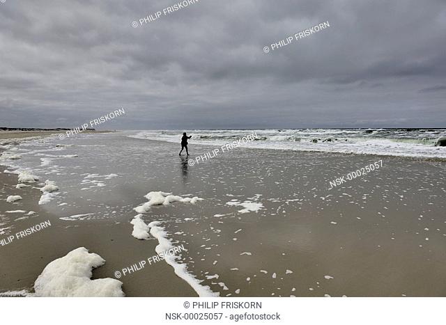 The beach of Terschelling with foam and silhouette of person, The Netherlands, Friesland, Terschelling