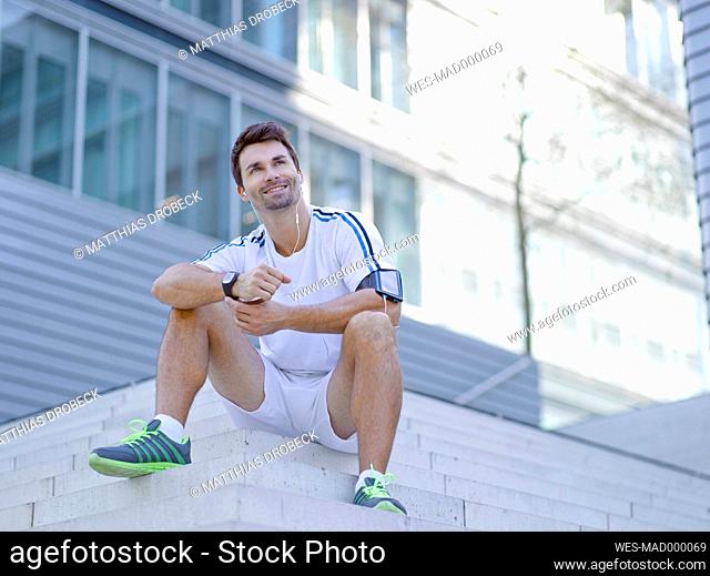 Smiling jogger with earphones sitting on stairs