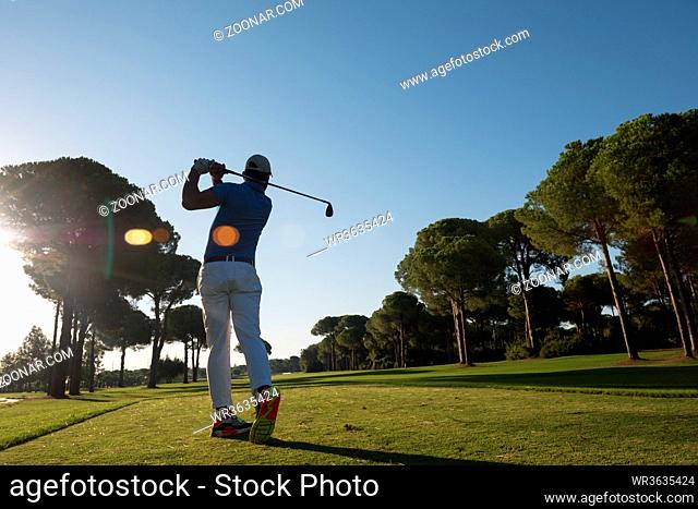 golf player hitting shot with club on course at beautiful morning with sun flare in background