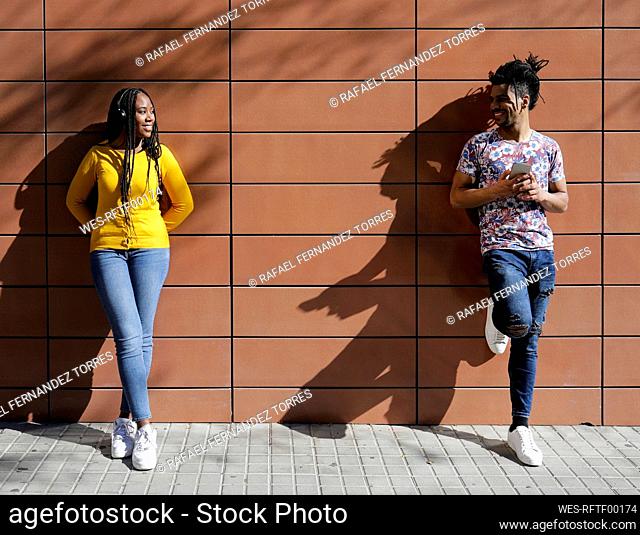 Smiling young couple looking each other in front of wall on sunny day