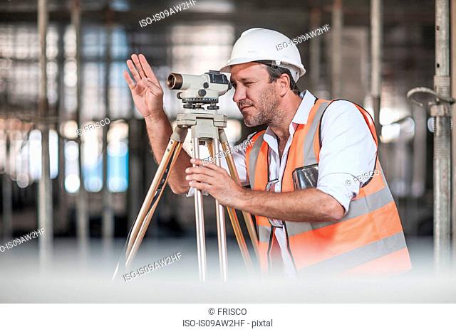 Male surveyor looking through theodolite on construction site