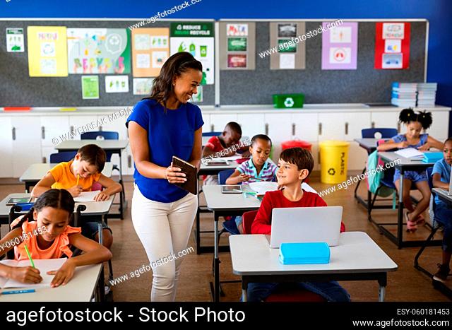 African american female teacher teaching caucasian boy to use digital tablet at elementary school