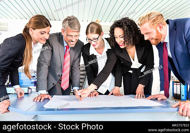 Group of business people are leaning over a desk and analyze graphs