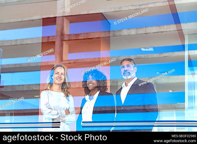 Entrepreneurs smiling while looking through window at modern office