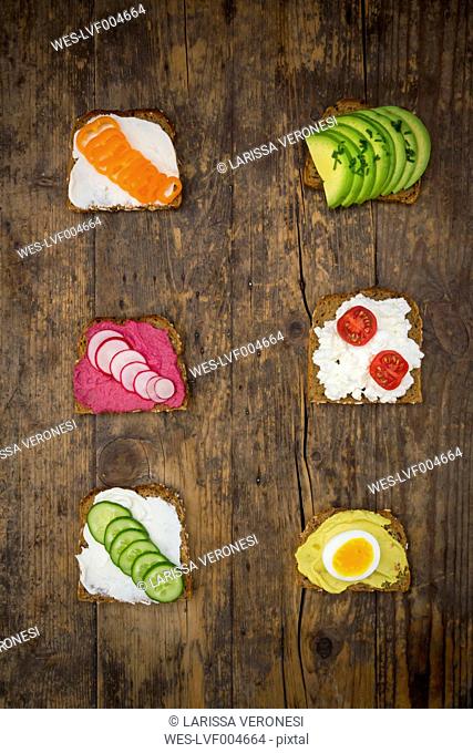 Wholemeal bread slices with different spreads and toppings on wood