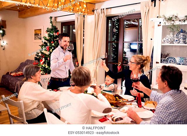 Beautiful big family sitting at the table, celebrating Christmat together at home. Illuminated Christmas tree behind them