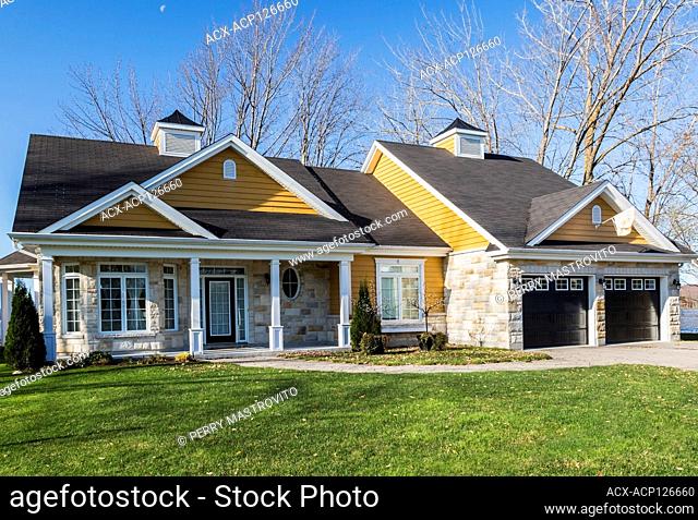 Country style house facade with tan and beige natural cut stone, yellow wood plank cladding and white and black trim in autumn, Quebec, Canada