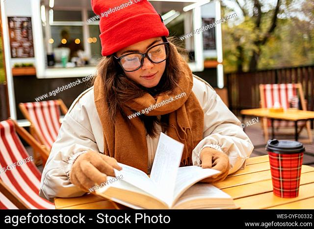 Young woman reading book while sitting at sidewalk cafe