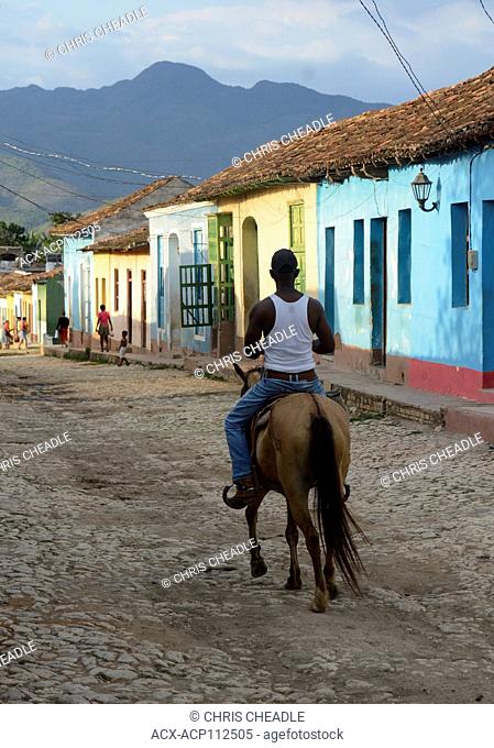 Resident man riding horse by colorful row of homes, Trinidad, Cuba