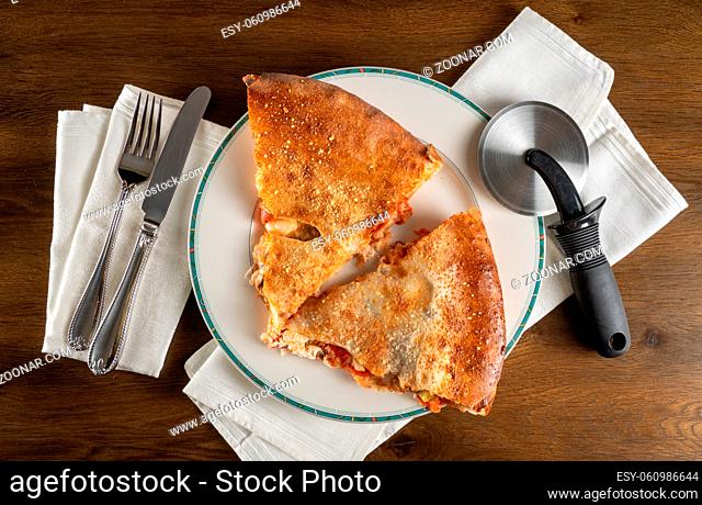 Layflat from above two slices from large double crust pizza with slicing tool and cutlery and white cotton napkins