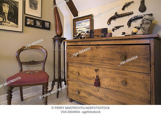 Antique wooden dresser, red upholstered chair on the upstairs hallway and walls decorated with paintings inside an old 1809 cottage style residential home