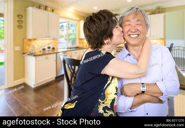 Happy senior chinese couple kissing inside beautiful custom kitchen