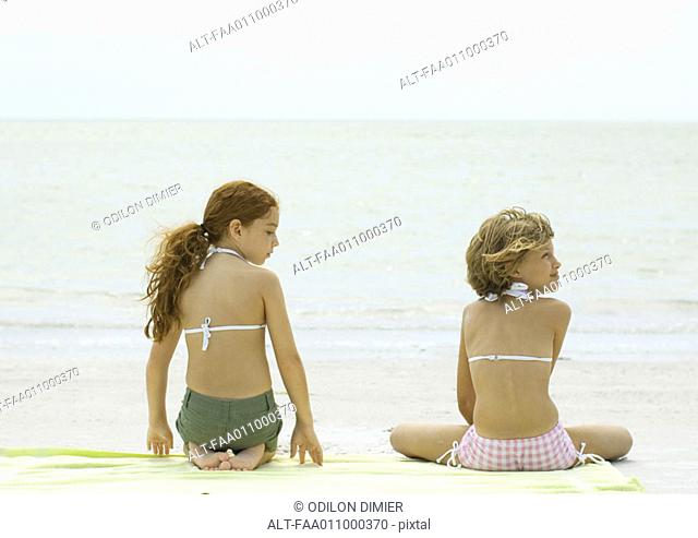 Two girls sitting on beach towel, rear view