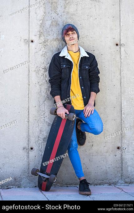Portrait of young and alternative boy standing with skate board and colorful clothes - modern people and youthful lifestyle - cement wall in background for city...
