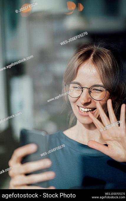 Happy businesswoman waving hand while doing video call through smart phone