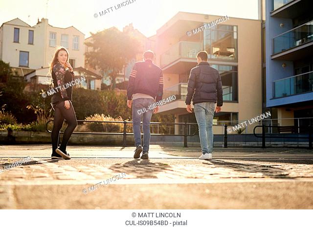 Three friends walking outdoors, young woman looking over shoulder, Bristol, UK