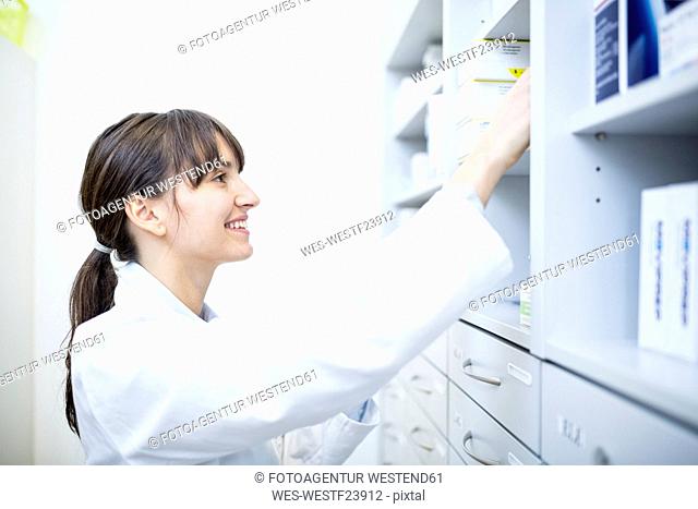 Smiling pharmacist checking medicine at cabinet in pharmacy