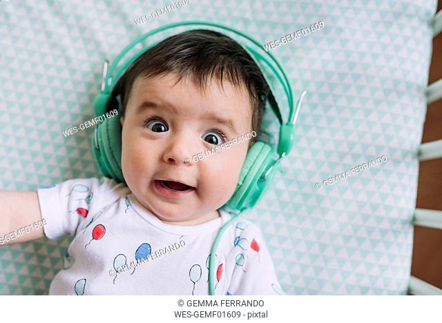 Portrait of baby girl with headphones lying in crib