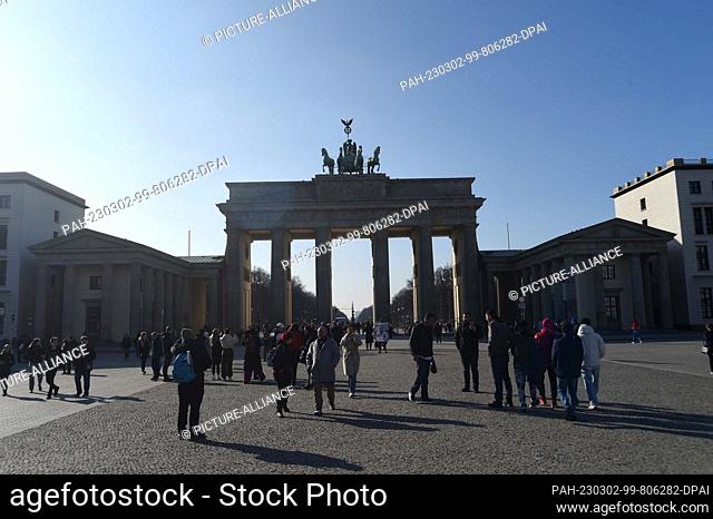 02 March 2023, Berlin: Tourists stand in front of the Brandenburg Gate under blue sky, cold temperatures and sunshine. Photo: Felix Hörhager/dpa