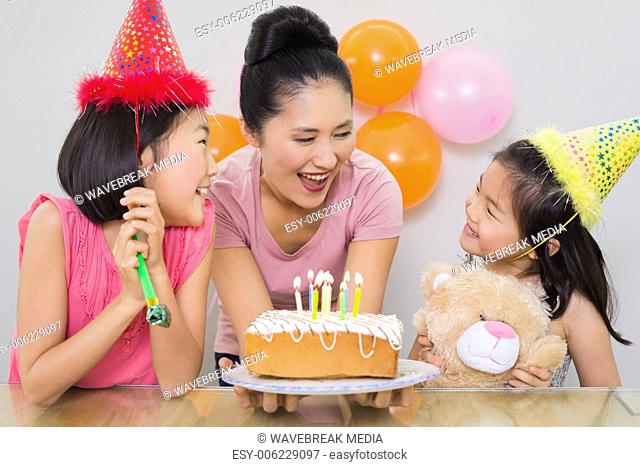 Girls looking at mother with cake at a birthday party