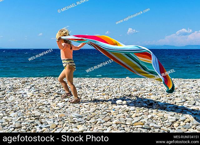 Little girl playing with towel on rocky beach