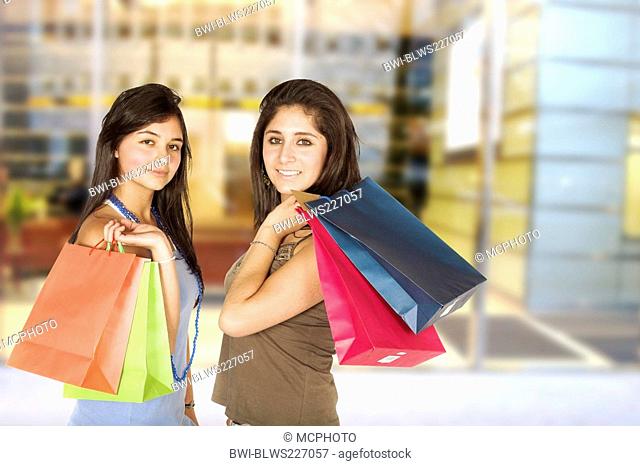 two smiling young woman with shopping bags over the shoulder in front of shopping centre