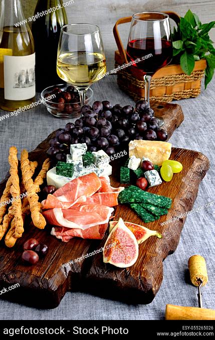 Dishes for a snack Antipasto on a wooden board with prosciutto, different kinds of cheese, grapes and figs on a table with wine