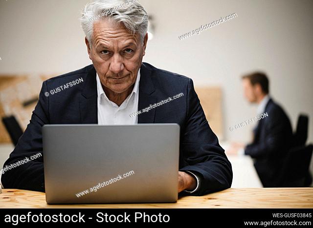 Senior businessman working on laptop, sitting in office with collueague