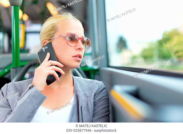 Blonde caucasian business woman talking on cell phone, traveling by bus. Public transport and commuting to work