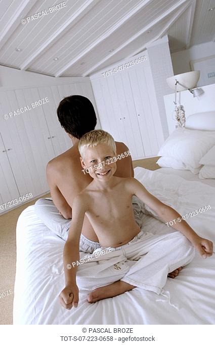 Portrait of a boy and his father sitting back to back on the bed