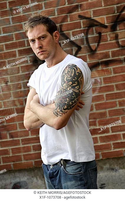 30 year old man standing alone with heavily tattooed arms