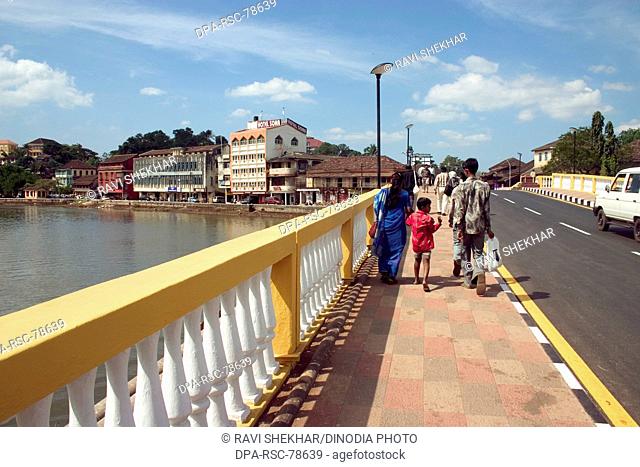 Old Pato bridge ;  Yellow bridge on Mandovi River ;  Mahatma Gandhi Road ;  blue sky ;  family walking on the bridge ;  old Portuguese structure of the Panjim...
