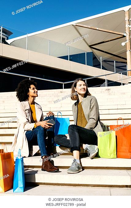 Two happy women with shopping bags sitting on stairs