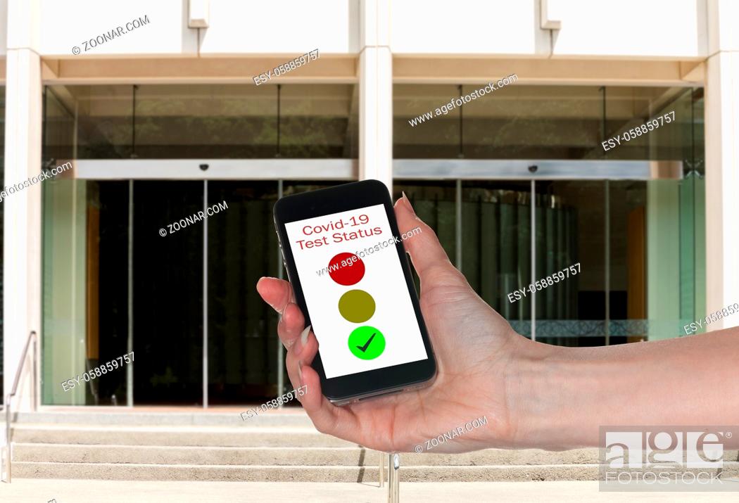 Stock Photo: Mockup of entrance to office with hand holding smartphone app showing immunity to coronavirus.
