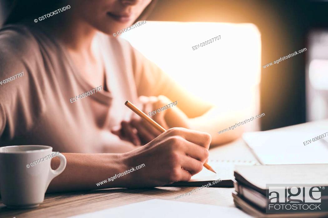 Stock Photo: Making some notes. Close-up part of young woman writing in notebook while sitting at her working place.