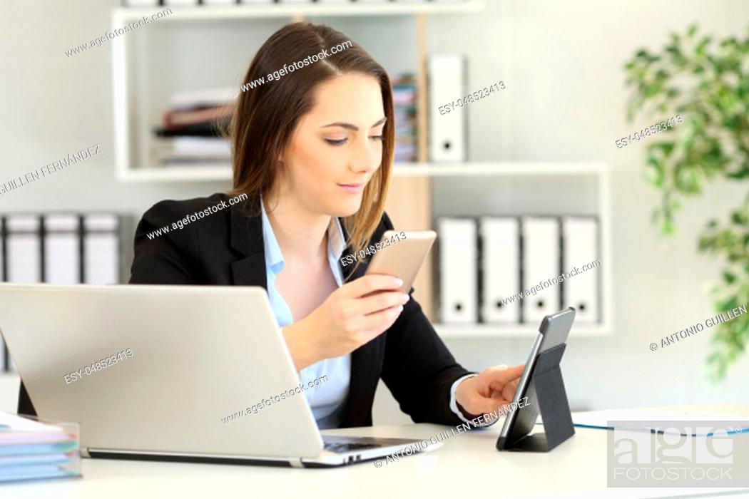 Stock Photo: Office worker working with multiple devices on a desktop.